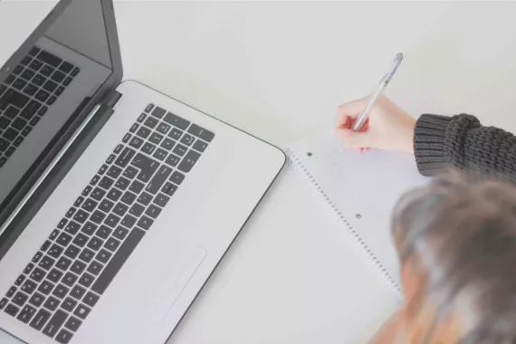 Woman making notes in front of a laptop